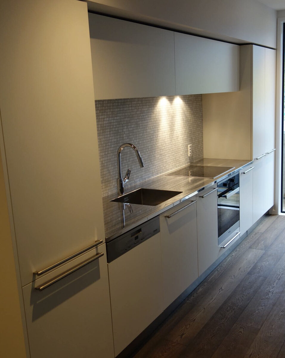 Linear white kitchen with mosaic splashback and timber flooring